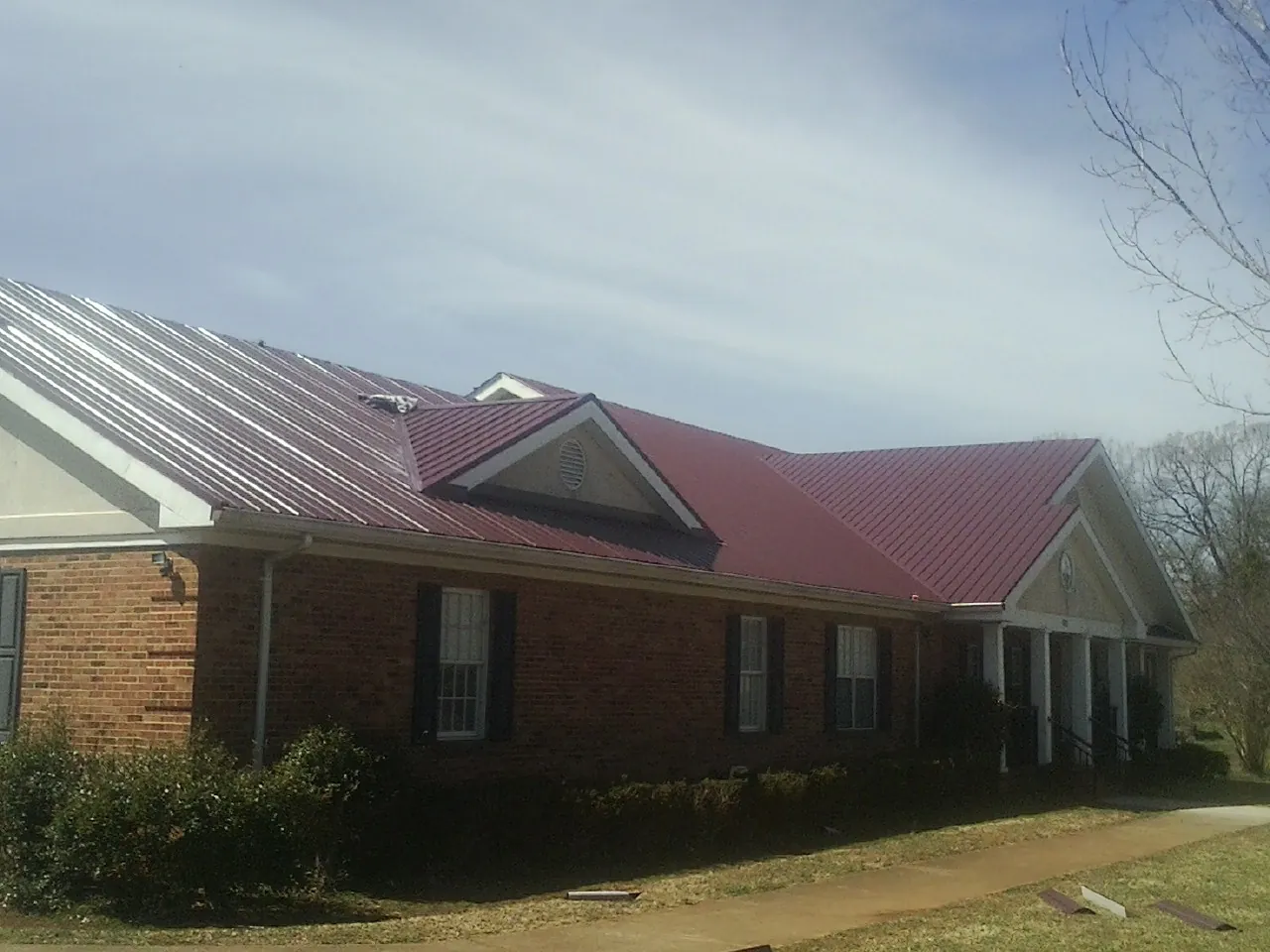 Red metal roof with gabled entries on a long brick building, from a Hail Damage Roof Repair job in Tarpon Springs