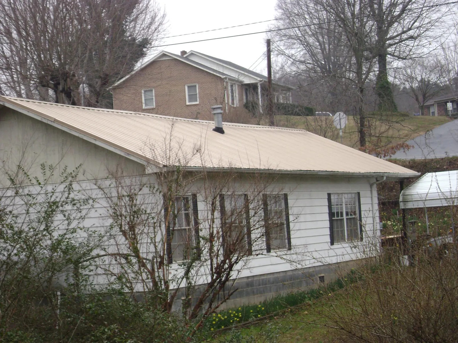 Tan metal roof on a white sided house set into a hillside — Commercial Roofing by Roofing Brothers in Tarpon Springs